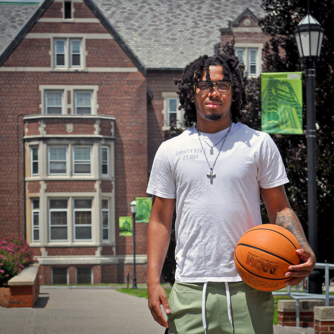 Photo of a male student with a basketball in front of a dorm